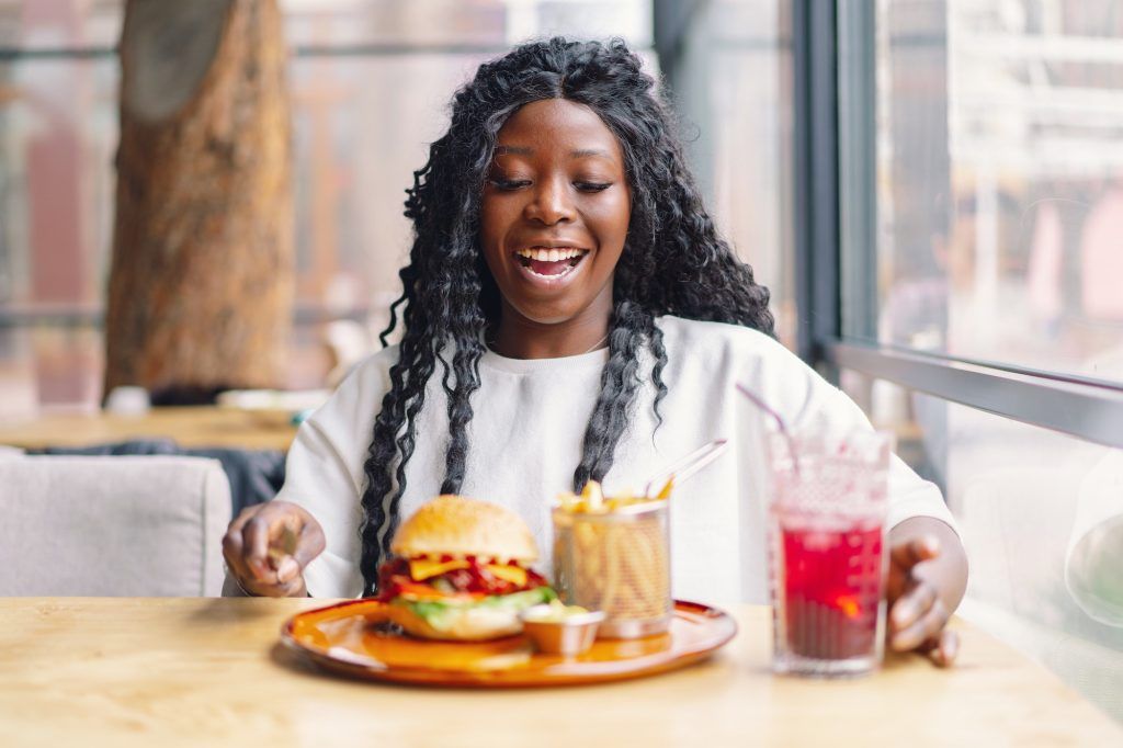 African woman with afro hair eating a tasty classic burger with fries. Cheat Meal.