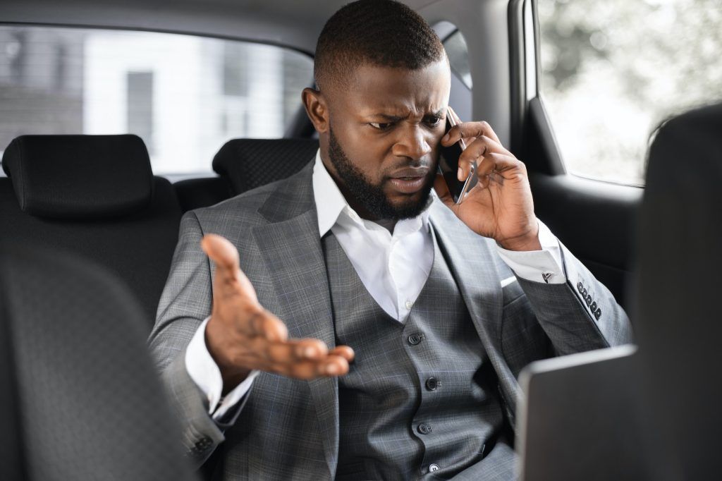 Angry african american businessman talking on phone in car