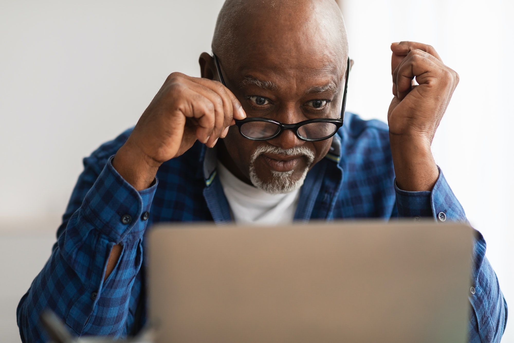 Shocked Senior African Man Looking At Laptop Above Eyeglasses Indoor