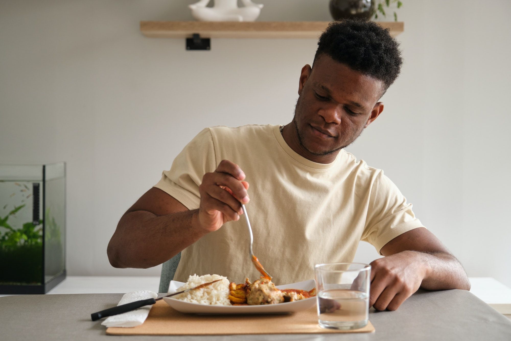 Young african man eating fried chicken, rice and plantain with tomato sauce.